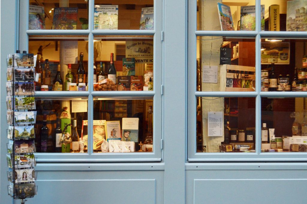 a shop front with sky blue decor showcasing various items for sale inside including postcards and drinks.