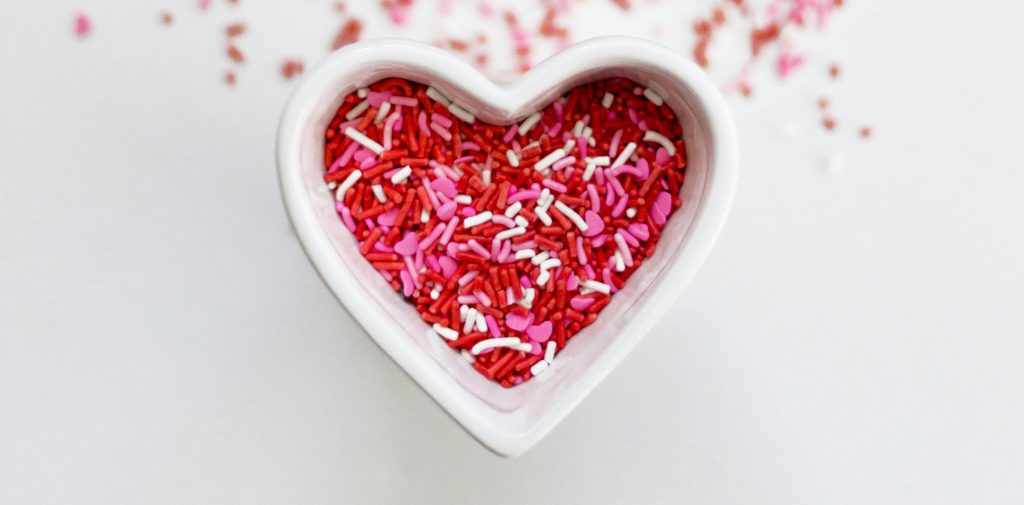 a small ramekin in the shape of a love heart filled with pink and red hundreds and thousands.